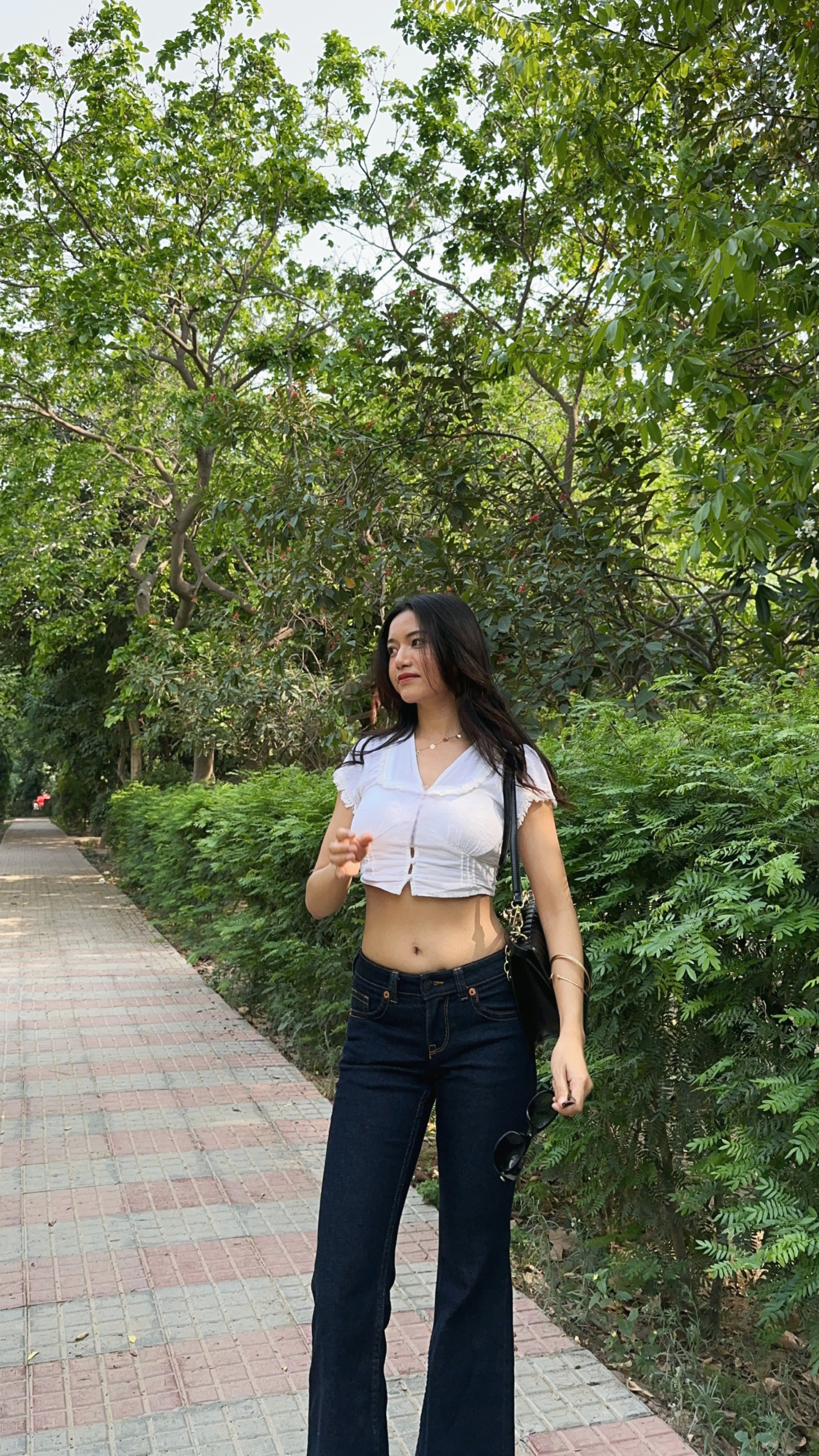 Jelina Derapi walking a tree-lined path in a white top and jeans, candid lifestyle moment